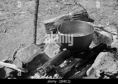 Zuppa turistica con verdure bolle in un calderone. Preparandosi su un fuoco aperto, pasto di campeggio. Foto in bianco e nero Foto Stock