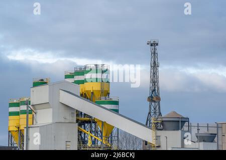 Cementificio con gru per il trasporto di materie prime. I silos in cui le materie prime vengono miscelate in cemento e i nastri trasportatori sono trasparenti Foto Stock