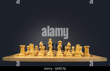 Pezzi di scacchi bianchi e neri con i pezzi bianchi in primo piano sono posti su una scacchiera. La tavola e i pezzi sono isolati in uno spazio grigio Foto Stock