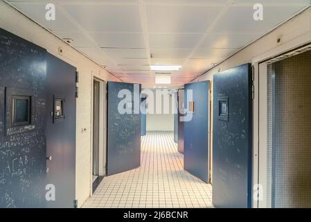 AMSTERDAM/PAESI BASSI-FEBBRAIO 24: Un corridoio vuoto di una prigione con piastrelle sul pavimento e porte a celle aperte in acciaio su cui i testi sono graffiati il ce Foto Stock