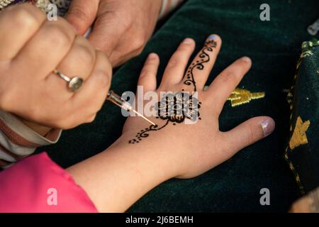 Artista che disegna un tradizionale tatuaggio henné mehndi in mano a una donna. Foto Stock