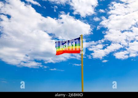 La bandiera nei colori della pace si getta sullo sfondo di un cielo blu nuvoloso. Simbolo di pace in questo tempo di guerra. pro concordia lavoro Foto Stock