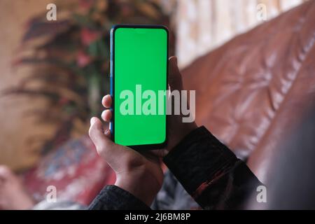 mano del giovane uomo che usa lo smartphone con schermo verde che giace sul divano Foto Stock