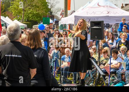 Downton, Salisbury, Wiltshire, Regno Unito, 30th aprile 2022. Downton Cuckoo Fair è tornato in un caldo sole primaverile glorioso dopo una pausa per la pandemia di Covid. L'evento popolare, con bancarelle di mercato e atti di strada, attrae una folla di migliaia di persone. I membri del coro Rock cantano il loro cuore. Credit: Paul Biggins/Alamy Live News Foto Stock