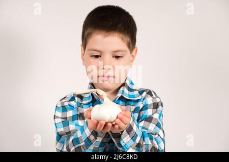 Un ragazzo di 4 anni tiene l'aglio su uno sfondo bianco. Verdure e vitamine per i bambini. Foto Stock