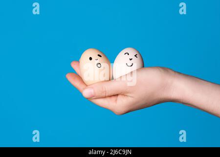 Mano che tiene due uova di pasqua con una faccia divertente disegnata su di esso. Pasqua o dieta sana mangiare concetto Foto Stock