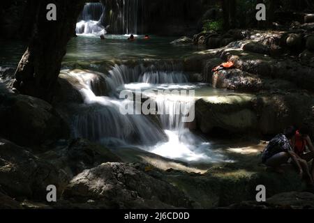 Cascata di cascate e rilassante persone su un fiume di montagna a Erawan Falls in Thailandia Foto Stock