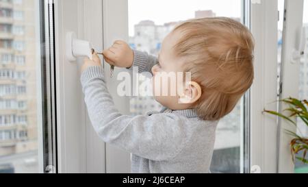 Il bambino apre la serratura di sicurezza della finestra con la chiave. Bambino in pericolo. Sicurezza e protezione dei bambini Foto Stock