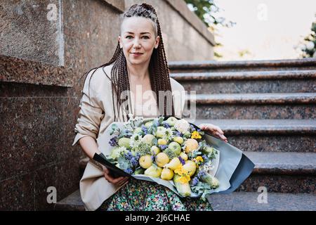 Consegna fiori. Giovane donna moderna hipster con dreadlocks che riceve bouquet di fiori bello dalla consegna all'aperto Foto Stock