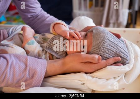 Una donna madre mette su una giacca calda per un bambino. La mamma indossa un bambino in abiti invernali sul letto. Foto Stock