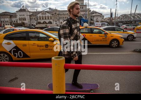 Mosca, Russia. 30th Aprile, 2022.Un giovane ragazzo corre uno skateboard sullo sfondo di taxi in piedi in jam traffico in Piazza Komsomolskaya nel centro di Mosca, Russia Foto Stock