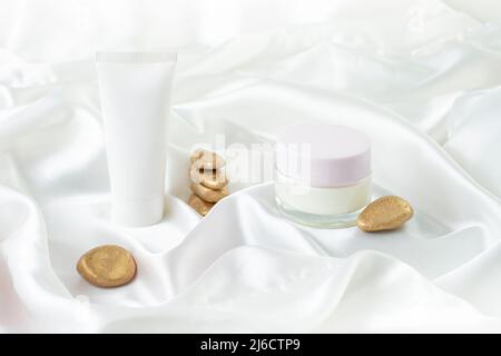 Provetta per crema mani e vasetto di vetro con spazio vuoto per l'etichetta su sfondo satinato bianco. Sfondo fotografico cosmetico del prodotto Foto Stock