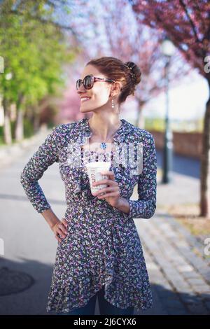 Felice giovane positivo rosso testa bianca donna che tiene il caffè all'aperto Foto Stock