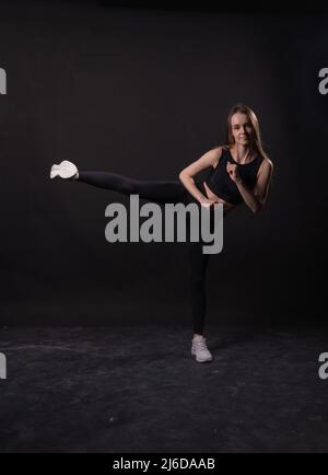 Sfondo nero calcia uno spago sulla ragazza A in karate marziale nero kimono, da blu studio in sport per la giovane arte, giappone attivo. Jujitsu femmina lotta Foto Stock