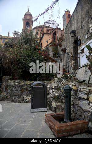 Chiesa e il suo campanile circondato da edifici visti da dietro e sotto una scogliera in una giornata nuvolosa Foto Stock