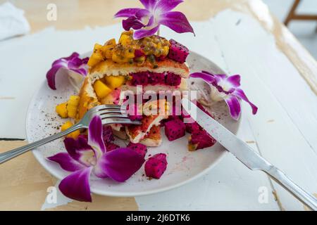 Gustosi pancake con frutta tropicale in un piatto su un tavolo in un caffè, primo piano. Colazione sana. Deliziosi pancake con mango, frutta di drago e pass Foto Stock
