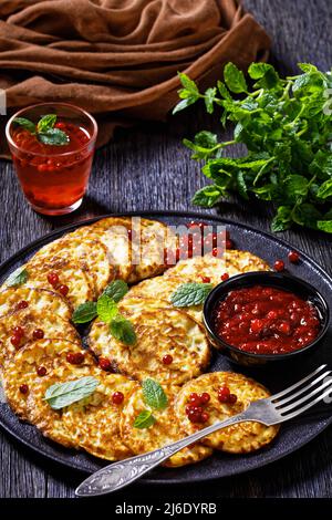 frittelle dolci di farine di farro con salsa di bacca, mirtillo di montagna, cowberry su piatto nero su tavolo di legno scuro, vista verticale dall'alto, primo piano Foto Stock