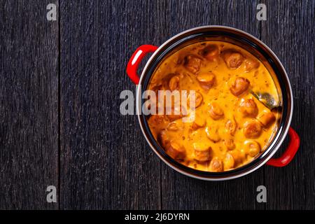 nakkikastike, salsicce finlandesi, amalgami in salsa di pomodoro cremosa in pentola rossa su tavola di legno scuro, vista orizzontale dall'alto, posa piatta, spazio libero, primo piano Foto Stock