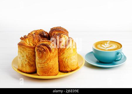 Dolci fatti in casa alla cannella da pasta di lievito e una tazza di cappuccino di caffè su tavola di legno bianco. Foto Stock