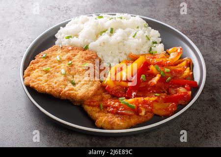 Schnitzel impanato in casa servito con salsa Gypsy di peperoni e cipolle con riso in un piatto su un tavolo. Orizzontale Foto Stock