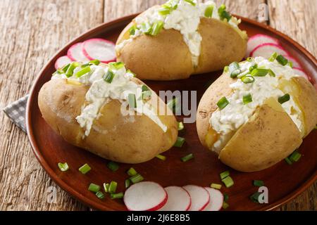 Patate deliziose con formaggio caserario, panna acida e cipolle verdi da vicino in un piatto su un tavolo di legno. Orizzontale Foto Stock