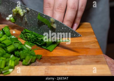 Primo piano delle mani che tengono le cipolle verdi su un tagliere di legno. Cottura di verdure in cucina. Ingredienti per la cucina. Foto Stock