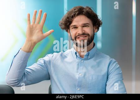 Concetto di saluto. Uomo d'affari sorridente che agitava la mano alla macchina fotografica Foto Stock
