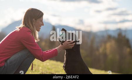 Giovane donna proprietario amorevolmente lodando il suo nero labrador Retriever tenendo un manichino - bella amicizia tra uomo e cane. Foto Stock