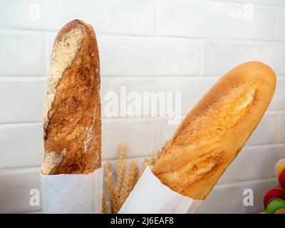 Primo piano due originali baguette francesi pane avvolto con carta su sfondo bianco parete. Foto Stock