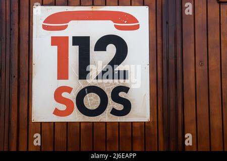 Primo piano di un cartello di emergenza con il numero di telefono 112 SOS, su sfondo di legno Foto Stock