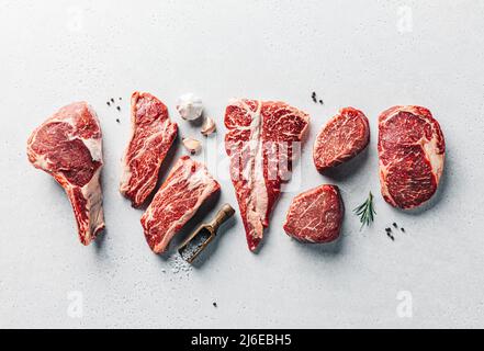 Varietà di bistecche di carne cruda con spezie su piano di cemento copia spazio. Ristorante grill Foto Stock