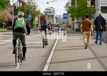Basilea, Svizzera - Aprile 2022: Le persone in bicicletta e a piedi a casa dal lavoro in una strada alla periferia del centro della città Foto Stock