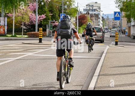 Basilea, Svizzera - Aprile 2022: Le persone che pedalano a casa dal lavoro in una strada alla periferia del centro della città Foto Stock