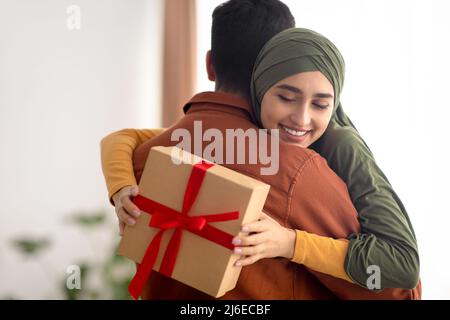 Coppia gioiosa Medio Oriente abbracciando Holding Gift Box in piedi al chiuso Foto Stock