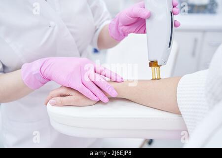 Cosmetologist che rimuove i capelli dal braccio femminile con dispositivo laser Foto Stock