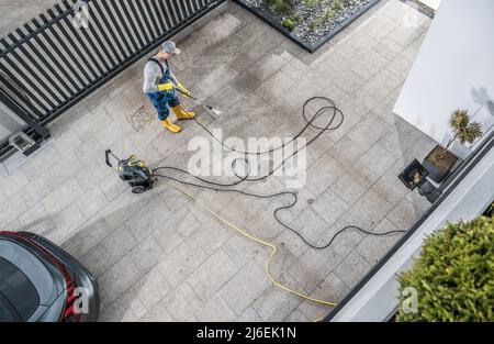 Casa caucasica Proprietario pressione Lavaggio il suo vialetto sporco Aerial Foto. Mantenendo mattoni di strada di cemento pulito. Foto Stock