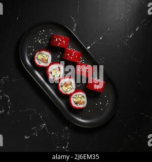 Tradizionale e delizioso sushi roll fresco su sfondo nero. Sushi roll con riso, nori, tobiko caviale, avocado. Menu di sushi. Cucina giapponese, res Foto Stock