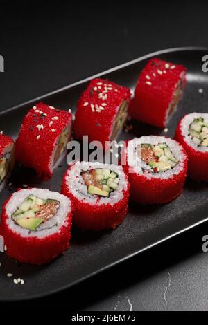 Tradizionale e delizioso sushi roll fresco su sfondo nero. Sushi roll con riso, nori, formaggio cremoso, caviale tobiko, avocado. Menu di sushi. Giapponese Foto Stock
