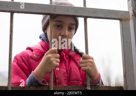 Foto di una bambina che tiene le barre. Ragazza piccola triste dietro le barre di ferro. Bambina dietro le sbarre. Concetto di violenza. Foto Stock