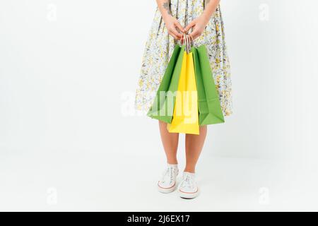 Da vicino giovane donna che indossa abiti e sneakers con pacchetti con acquisti mentre si alza su sfondo bianco studio Foto Stock