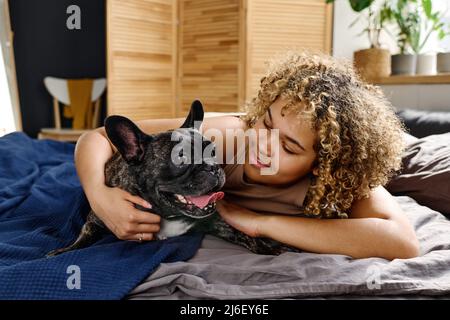Ritratto di donna sorridente felice con il suo carino bulldog francese sdraiato a letto al mattino Foto Stock
