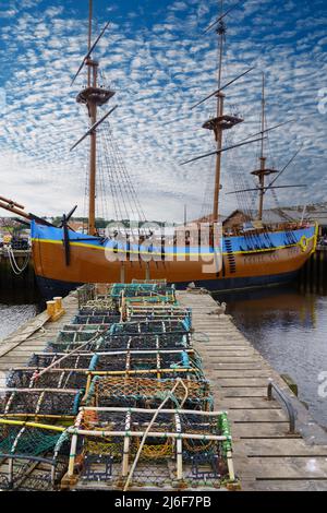 Un molo di legno con file di pentole di aragosta che si asciugano insieme a una replica della nave del Capitano Cook, HMS Endeavour, Whitby, North Yorkshire, Inghilterra, REGNO UNITO. Foto Stock