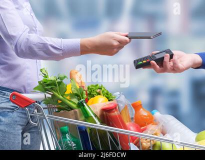 Donna che paga per generi alimentari utilizzando il suo smartphone, NFC Payments Concept Foto Stock
