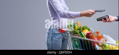 Donna che paga per generi alimentari utilizzando il suo smartphone, NFC Payments Concept Foto Stock