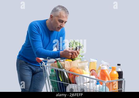 Uomo che spinge un carrello e utilizza uno smartphone, negozi di alimentari e tecnologia concetto Foto Stock