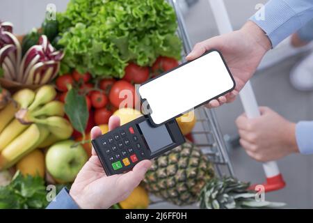 Donna che spinge un carrello completo per la spesa e paga per i generi alimentari con il suo smartphone, concetto di pagamenti mobili, vista dall'alto Foto Stock