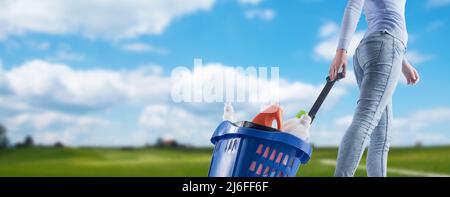 Donna che tira un carrello pieno di prodotti per la pulizia e verde paesaggio sullo sfondo Foto Stock