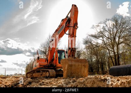 Un escavatore con benna scava una trincea per la posa di tubi. Veicolo da costruzione. Costruzione. Tubo di scarico Foto Stock