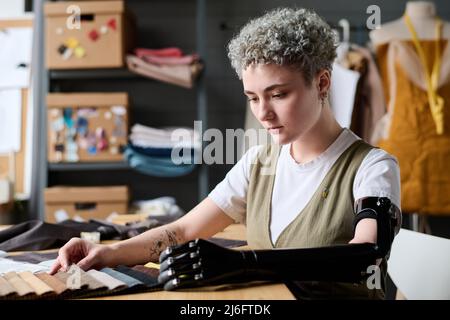 Designer di moda contemporaneo e serio che guarda attraverso i campioni di colore del tessuto mentre sceglie alcuni per la nuova collezione stagionale Foto Stock