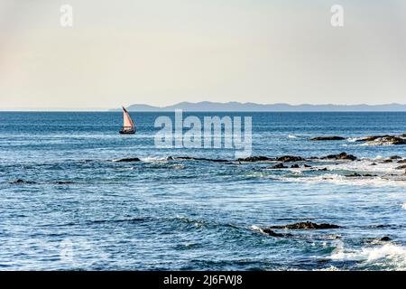 Rudimentale barca da pesca che naviga attraverso le acque calme della baia di Todos os Santos nella città di Slavador a Bahia durante il tramonto Foto Stock